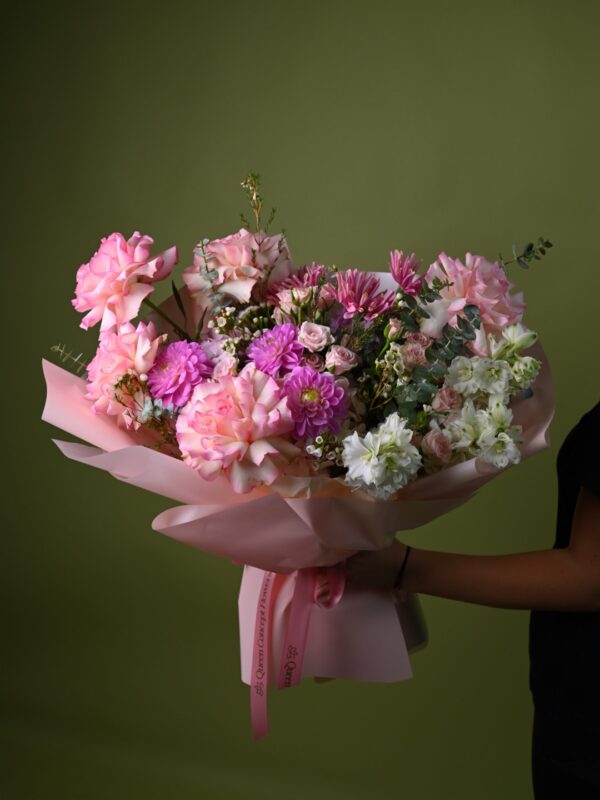 Buchet romantic cu trandafiri roz cu margini îndoite, dalii mov și delphinium alb, în ambalaj roz pudrat