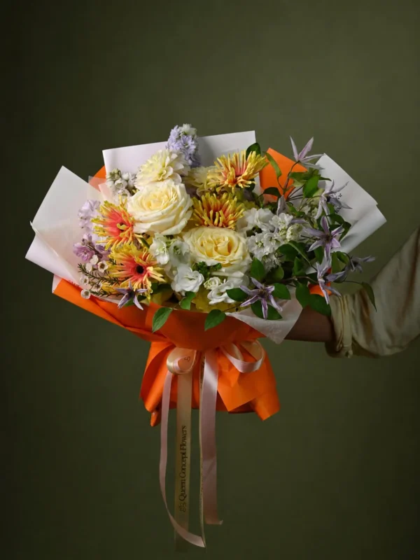 Buchet cu trandafiri crem, gerbera portocalie, delphinium alb și clematis mov, în ambalaj alb cu portocaliu